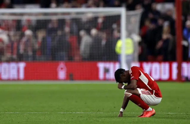 Elanga crouches down on the turf and puts his fist to his head in frustration.