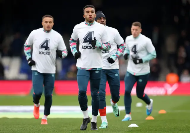 Jacob Brown of Luton Town warms up alongside teammates whilst wearing a warm up shirt in support of teammate Tom Lockyer prior to the Premier League match between Luton Town and Newcastle United