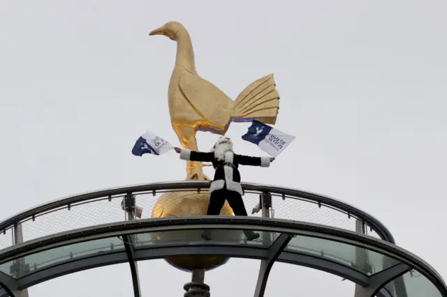 A santa caus dressed in tottenham navy waves flags from the roof of the stadium.