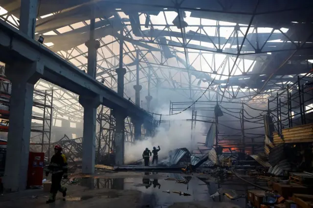 Firefighters work inside a warehouse hit by a Russian missile, the building is on fire