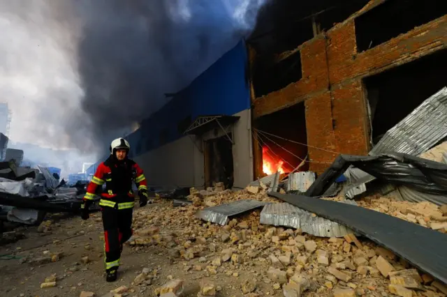 A firefighter walks outside a warehouse hit by a Russian missile, the building is on fire