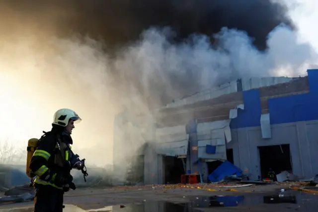 A firefighter stands outside a warehouse hit by a Russian missile, the building is on fire