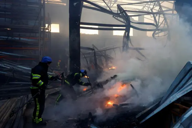 Firefighters work inside a warehouse hit by a Russian missile, the building is on fire