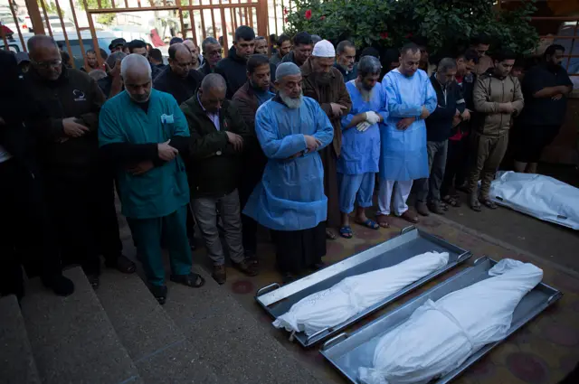 Relatives of Palestinians from the Abu Najili family, who died during Israeli air strikes in the southern Gaza Strip, pray along with medical staff in front of their wrapped bodies, outside Nasser Hospital in Khan Younis