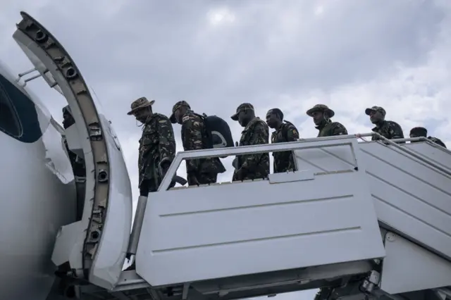 Uniformed Kenyan soldiers board a plane going back to Kenya.