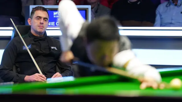 Ronnie O'Sullivan watches Ding Junhui at the table