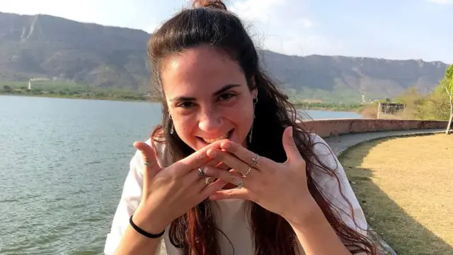 Inbar Haiman covers her mouth as she grins next to a body of water