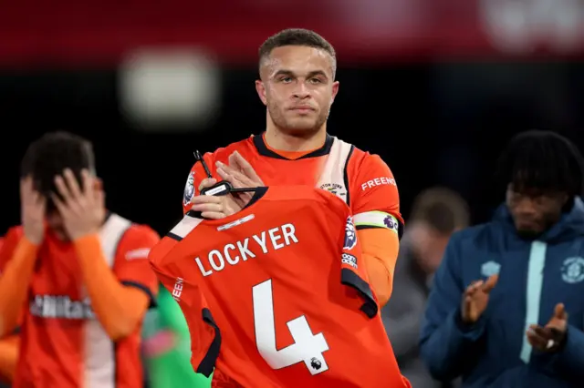 Carlton Morris of Luton Town applauds the fans whilst holding the shirt of teammate Tom Lockyer after the team's victory in the Premier League match between Luton Town and Newcastle United