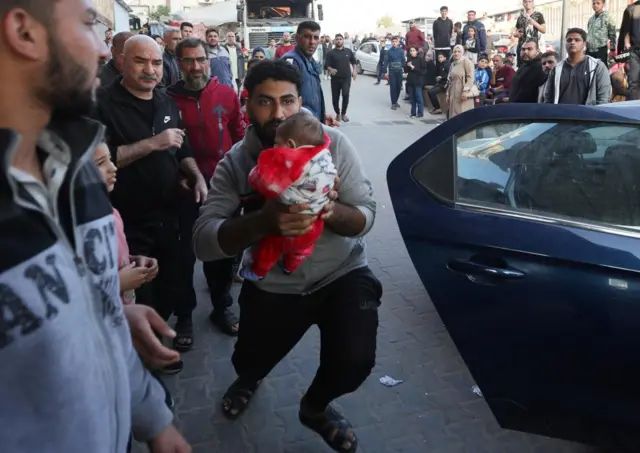 A man carrying a baby arrives at Nasser Hospital