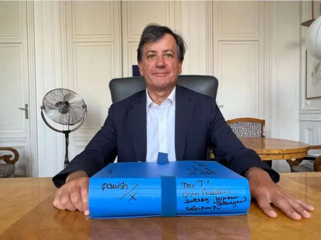 Didier Seban sitting at his desk with a folder of documents