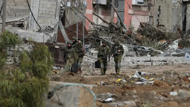 Four soldiers walk past mounds of rubble