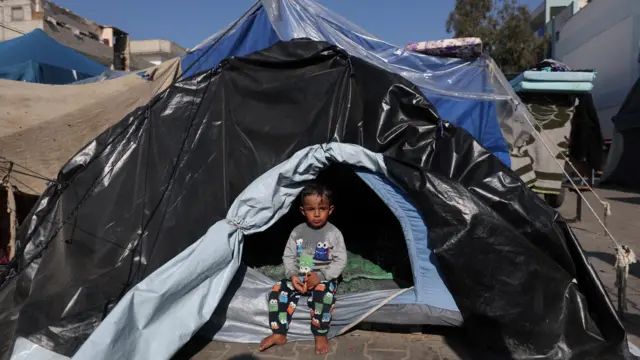 A child sits in a tent as Palestinians, who fled their houses amid Israeli strikes, shelter at a United Nations-run school, amid the ongoing conflict between Israel and the Palestinian Islamist group Hamas, in Khan Younis