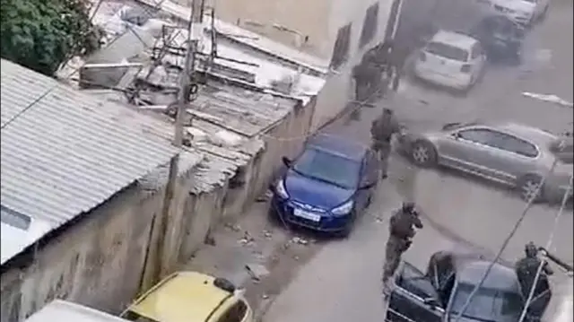 Three Israeli soldiers aim their guns down a street