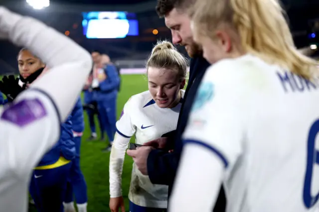 England players gather around a phone for news of another game.