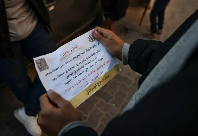 A Palestinian holds a leaflet dropped by Israeli forces, urging residents to leave areas of Khan Yunis