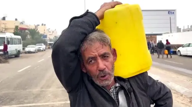 Man walks down a road carrying a water tank on his shoulder