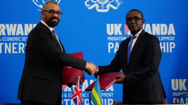 Cleverly and Biruta shake hands as they hold up red folders