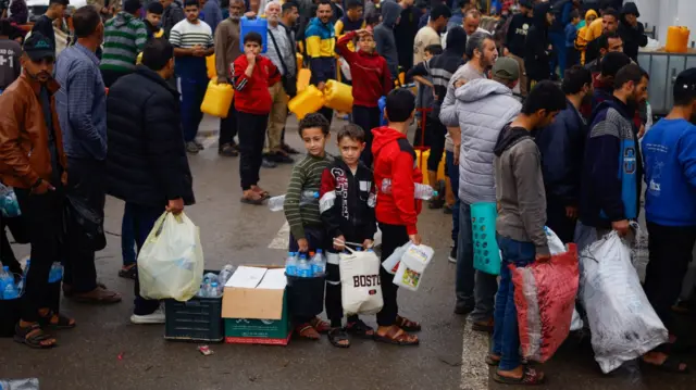 Palestinian children queue to collect water amid shortages during the ongoing conflict