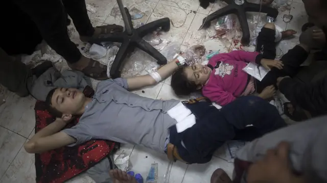 Two children lie on the blood covered floor of a hospital with bands and wires on their wrist