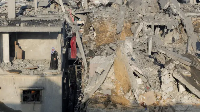 A Palestinian woman stands in a destroyed room in a building as she inspects the site of Israeli strikes in Khan Younis