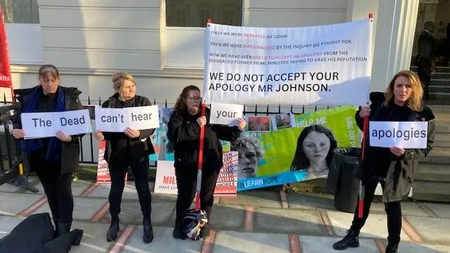 Four protesters carry pieces of paper reading "The Dead can't hear your apologies"