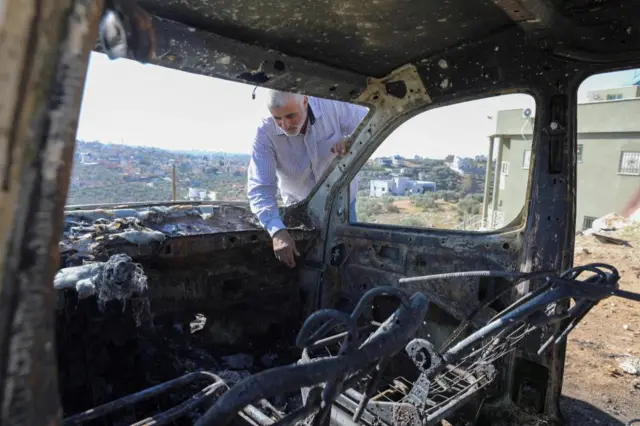 A Palestinian checks a car burned in Israeli settlers' raid near Salfit in the Israeli-occupied West Bank