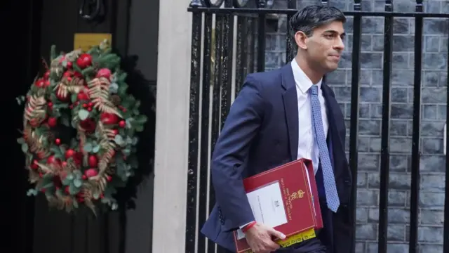 Sunak holds a red folder, walking past the door of Number 10