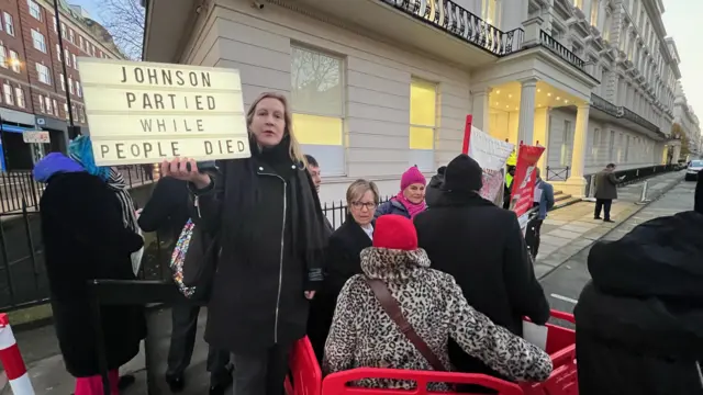 Protestors holds sign saying "Johnson partied while people died"