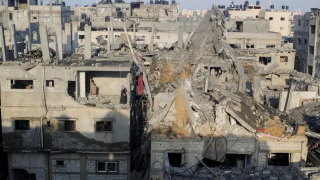 A Palestinian woman stands in a destroyed room in a building as she inspects the site of Israeli strikes