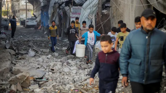 Palestinian children carry items as they walk at the site of Israeli strikes in Khan Younis