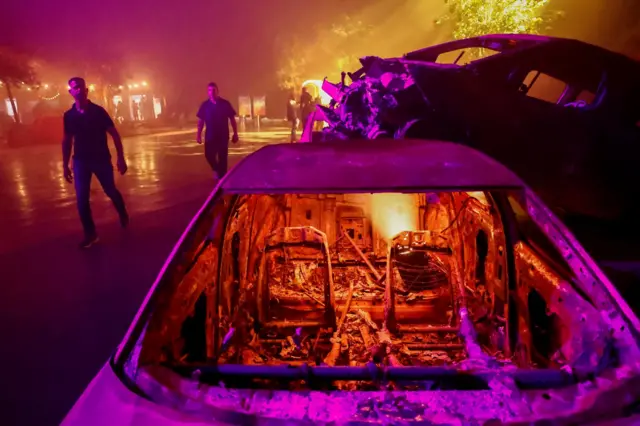 People in Tel Aviv walk past burnt cars as they view an exhibit that reconstructs the Supernova music festival grounds. Photo: 6 December 2023