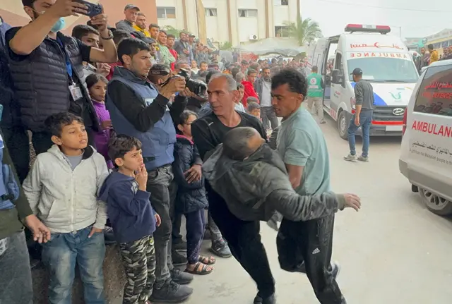 People rush a man into hospital next to an ambulance and a crowd of people, taken in Khan Younis on 7 December