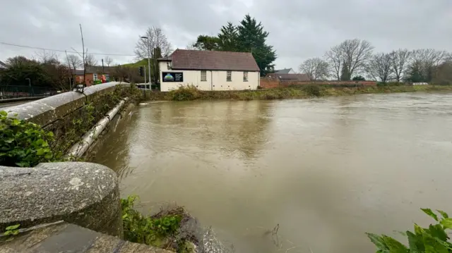 A swollen river passing underneath a stone bridge