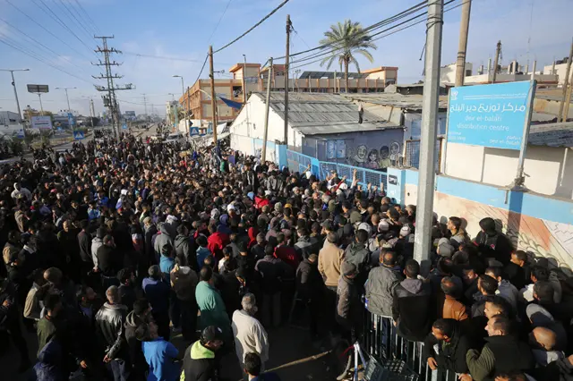 A crowd of people line up to receive flour being distributed by the UN Agency for Palesilian Refugees (UNRWA), in Deir al-Balah on 7 December