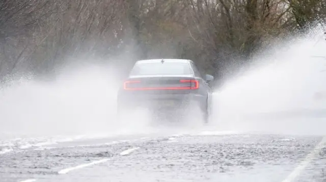 A car being driven through surface water on a road