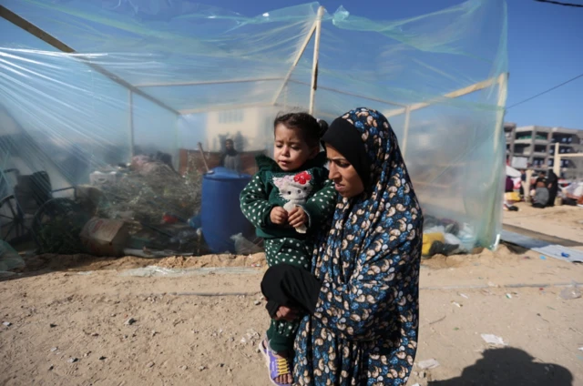 A woman holds a child while sheltering in a camp in Rafah, 6 December 2023