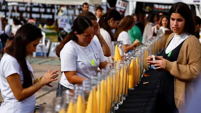 Row of yellow candles being lit by women