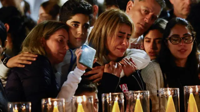 Families of hostages stand by a line of lit candles