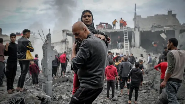 A man carries a young woman outside damaged buildings, Khan Younis, 7 December