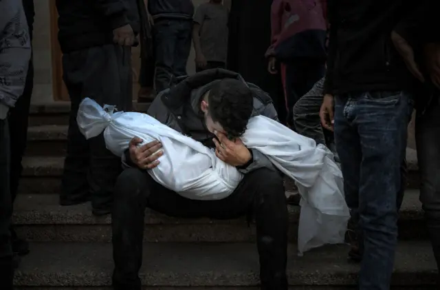 Man holds a small body wrapped in a white sheet, in Khan Younis, 7 December