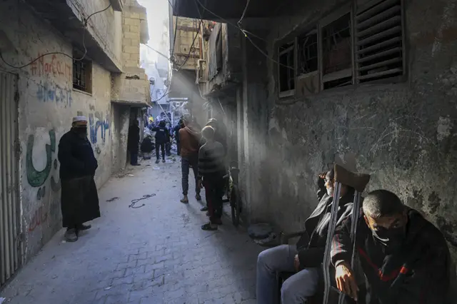 People gather in an alleyway with sun shining through, in Rafah on 7 December