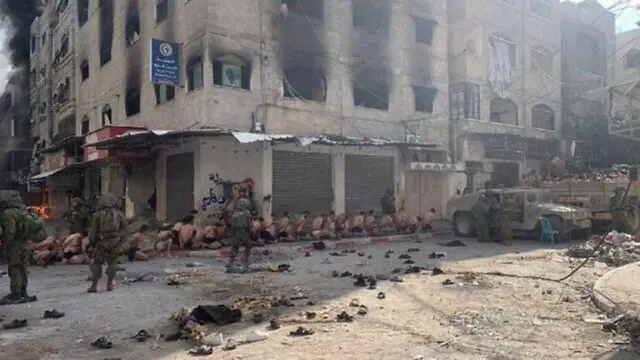 Still from a video circulating on social media showing dozens of Palestinian men, stripped to their underwear, kneeling on the ground, being guarded by Israeli soldiers, along the side of a damaged building.