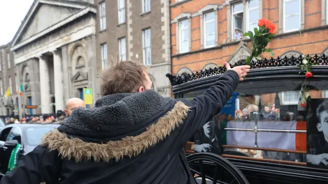 A man throws a rose onto the cortege