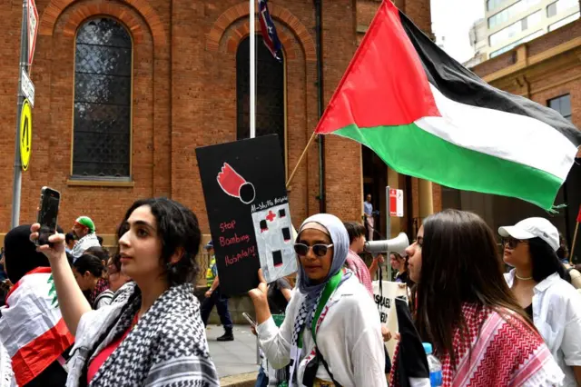 Pro-Palestinian protesters march in Sydney on Thursday. One is holding a placard that reads: "Stop bombing hospitals". Another is waving a Palestinian flag.