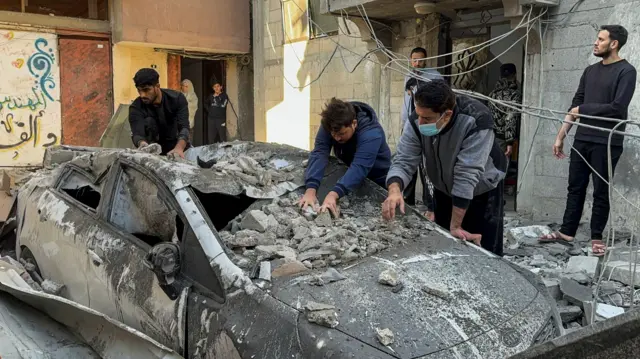 Palestinians remove rubble from a damaged car