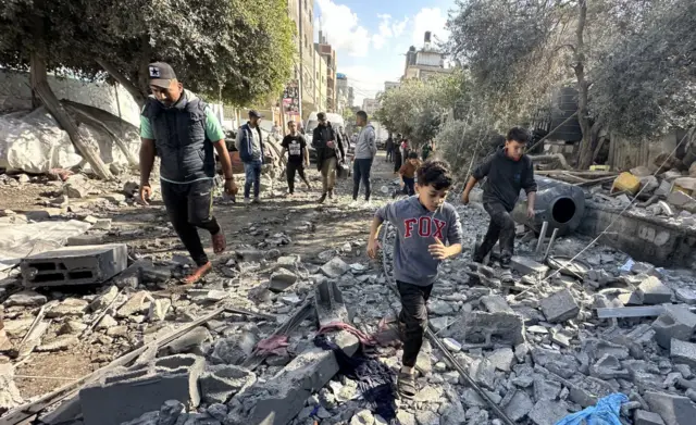 Residents and civil defense teams conduct a search and rescue operation around the rubble of the building that collapsed following an Israeli attack