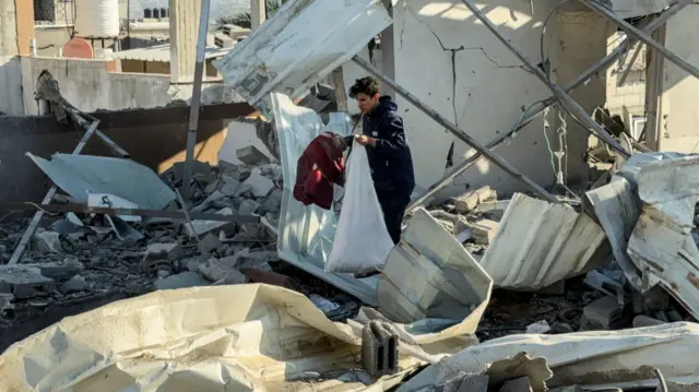 A Palestinian man gathers belongings among the rubble at a site of an Israeli strike