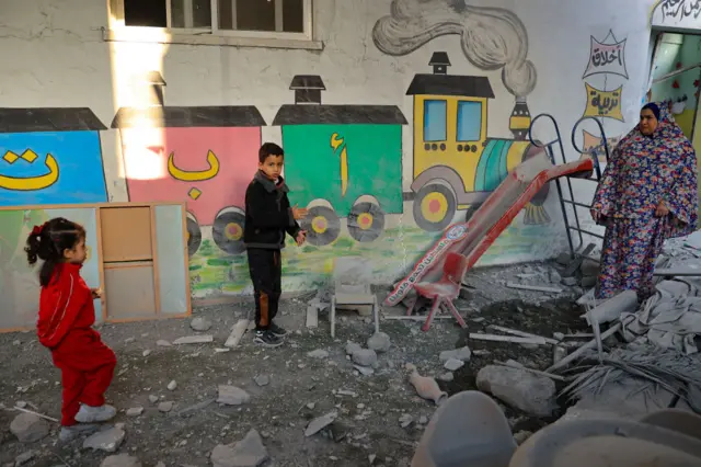 A woman and children stand amid the rubble at a nursery