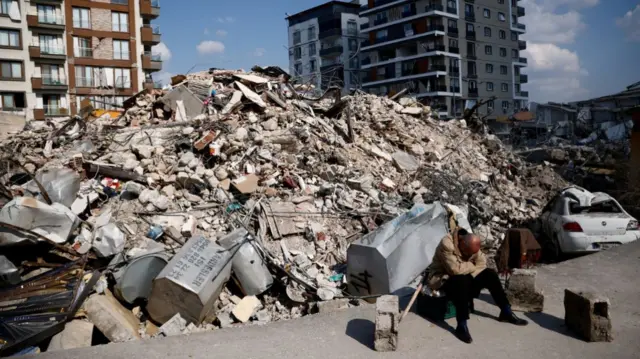 A man sits next to rubble at the site of a collapsed building in the aftermath of a deadly earthquake in Antakya, Turkey