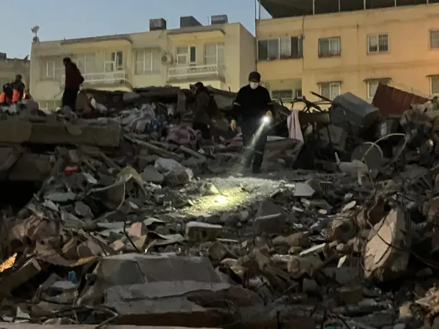 Person holds a torch searching rubble